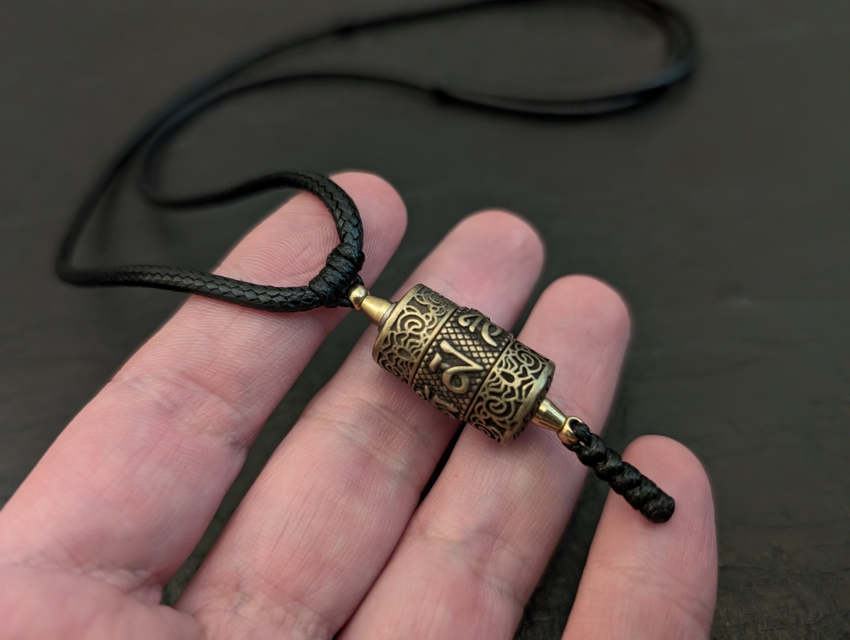 Tibetische Gebetsmühle als Anhänger aus Bronze mit dem Mantra Om Mani Padme Hum in der Hand